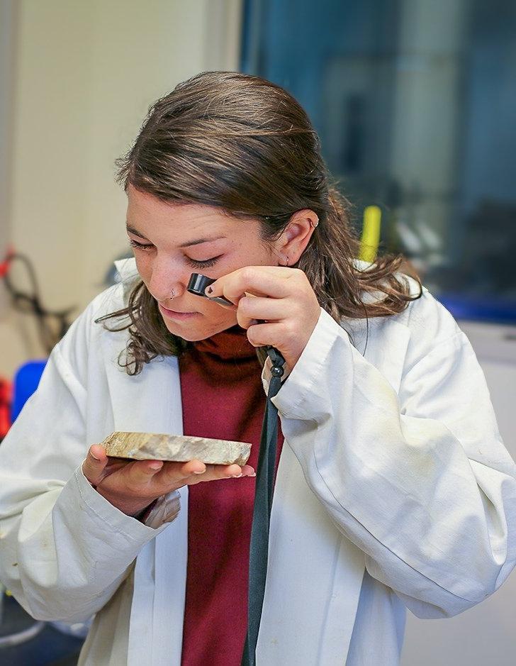 a student uses a loupe to study an artifact