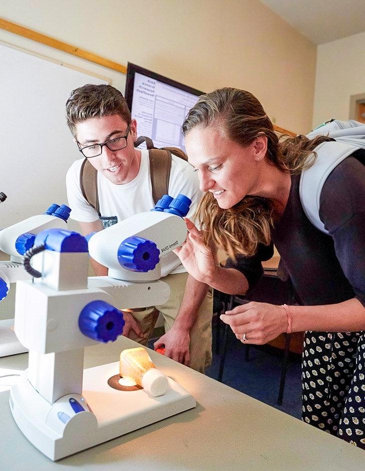 two students peer into a microscope in a classroom